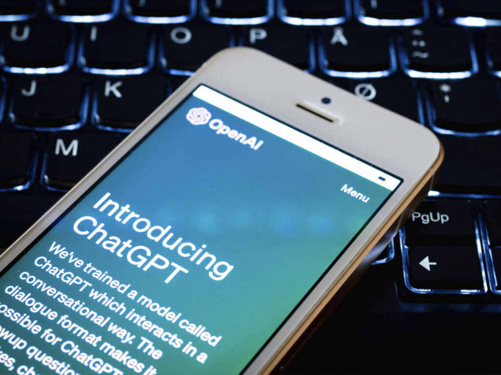 A smartphone displaying the OpenAI ChatGPT introduction homepage resting on a backlit computer keyboard.