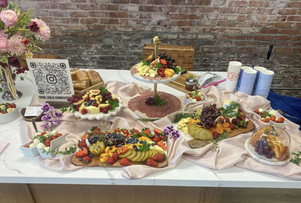 Elegant Rose Gold Charcuterie grazing table with meats, cheeses, fresh fruit, bread, and floral accents.